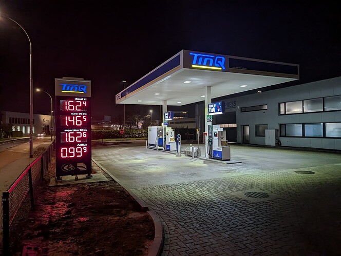 TINQ opened before Tesla Supercharger 1 Photo taken in the dark showing that the gas pumps are working because the displays are lit up nicely. Prices are displayed on the large illuminated column on the side of the road